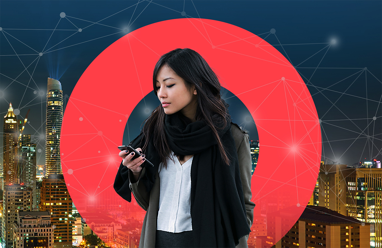 Businesswoman looks at her phone on a rooftop overlooking night cityscape.