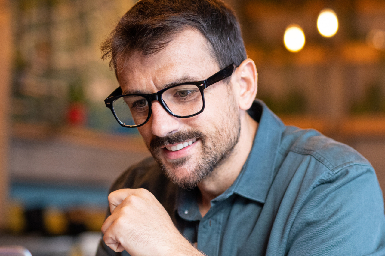 A man smiles as he looks down towards a screen, appearing intrigued. 