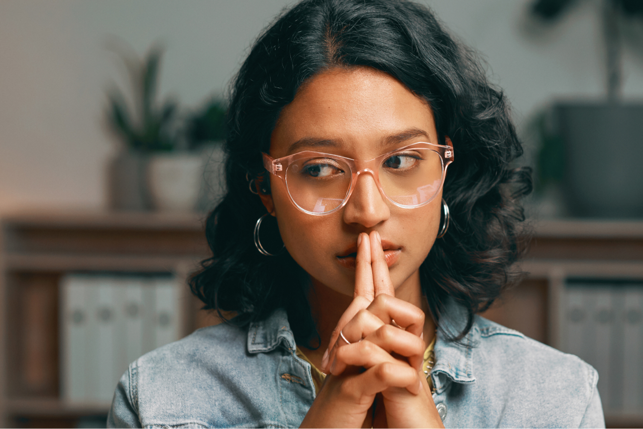 A woman places her crossed hands in front of her face and looks to the side, appearing stressed or overwhelmed.