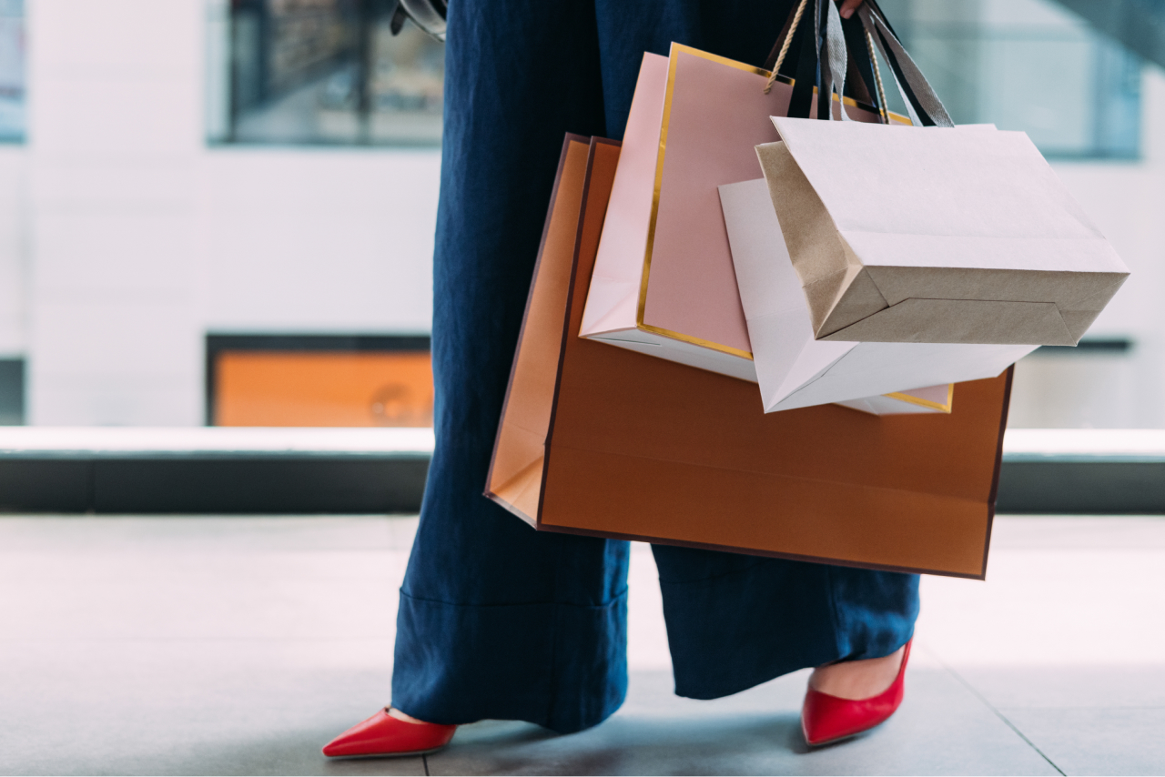 A woman's lower body in red heels, walking on the street while carrying several shopping bags.