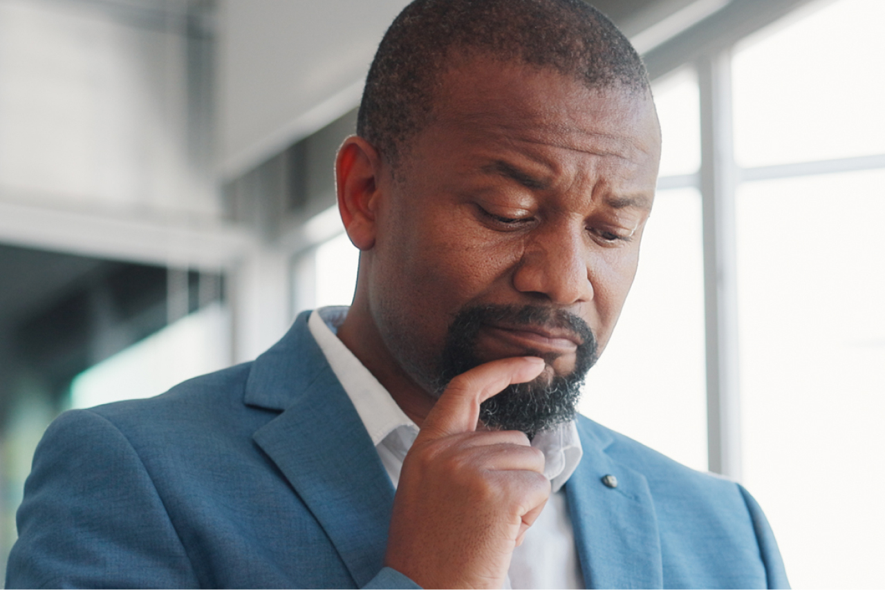 A man in a suit with his finger on his chin, appearing perplexed. 